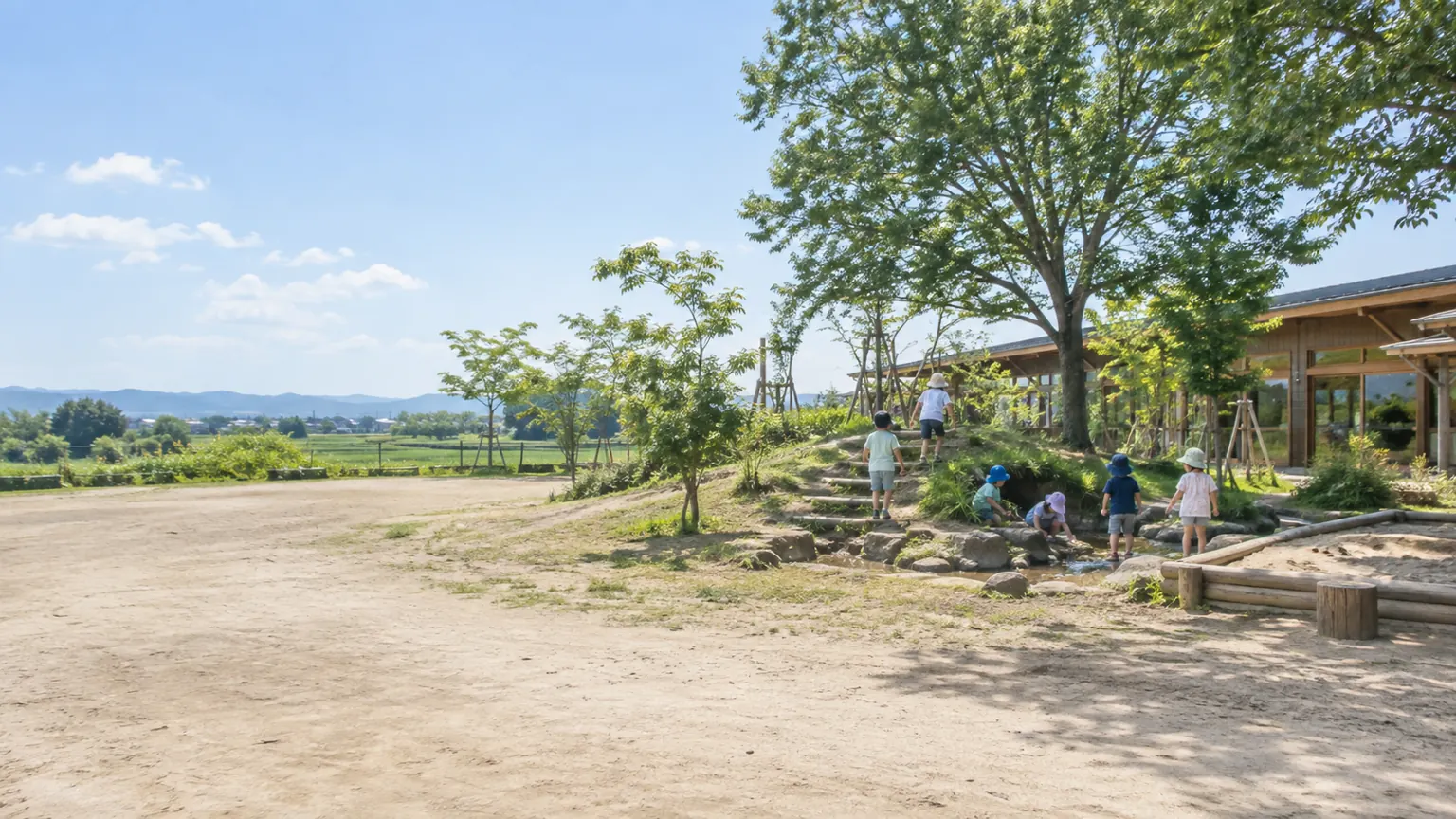 園庭のすみの築山と小川で遊ぶ子どもたちの後ろ姿