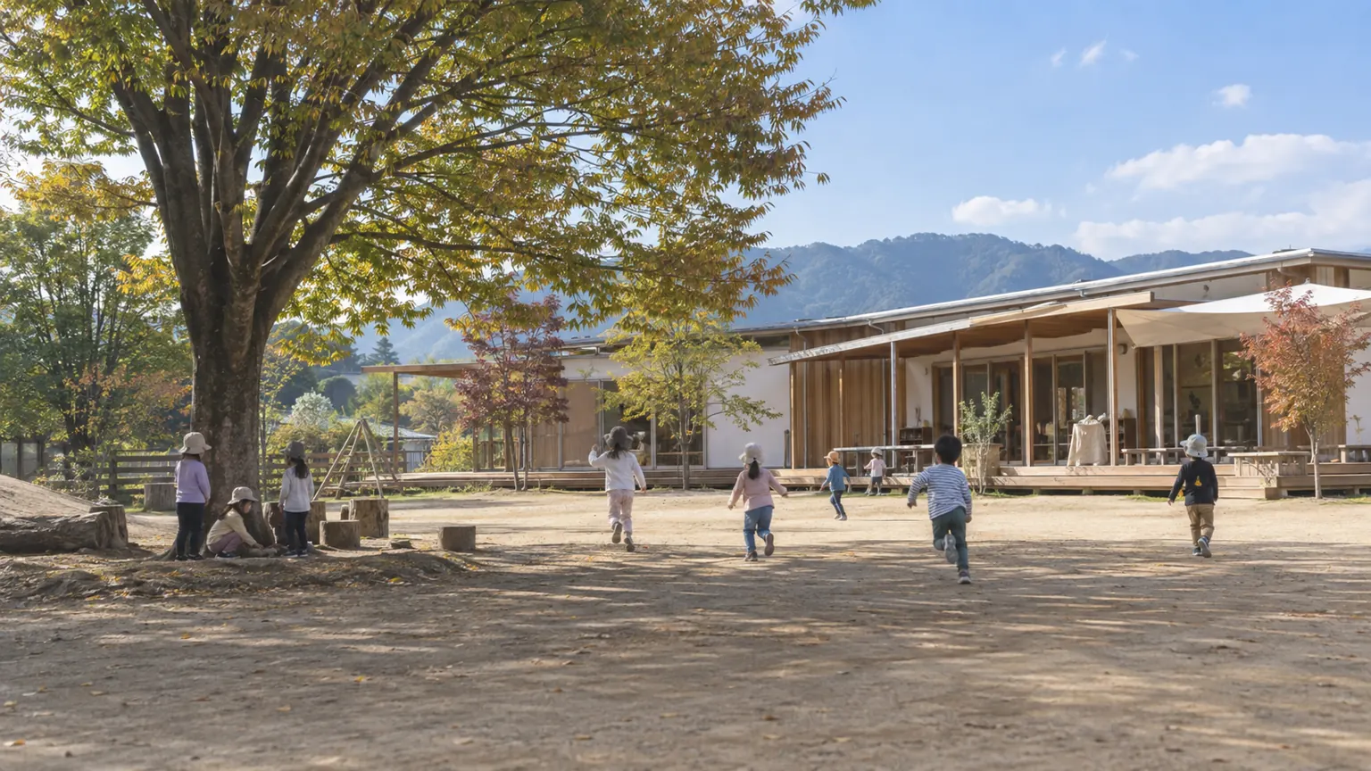秋の園庭で走る子どもたちの後ろ姿と、木の園舎
